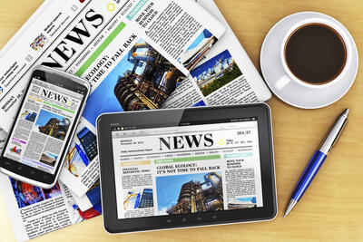 Creative business corporate work concept: tablet computer PC, modern black glossy touchscreen smartphone with news internet web site, stack of newspapers, cup or mug of fresh coffee and metal ballpoint pen on wooden office table
