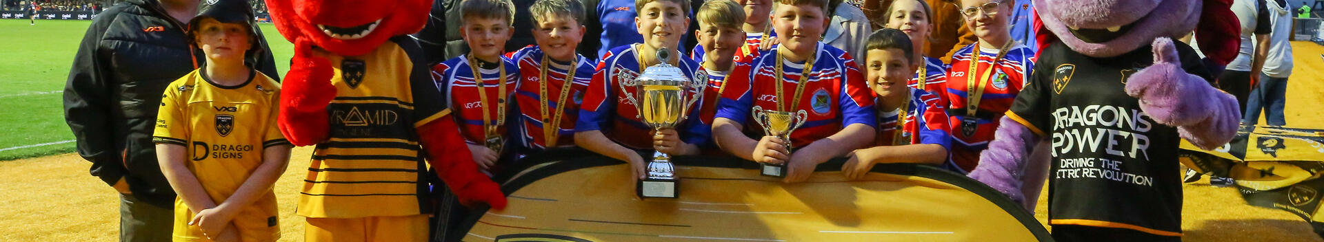 Children from Ystrad Mynach Primary School celebrate after winning the Tata Steel – Phil James Memorial Cup Final alongside Dragons RFC Community representatives.