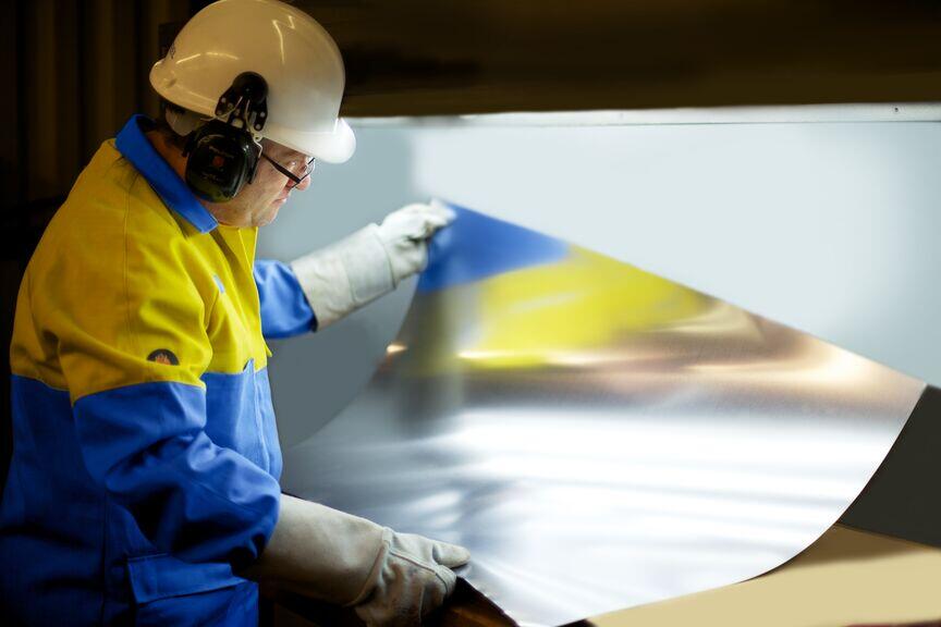 Packaging steel sheet being examined by Tata Steel employee wearing protective equipment