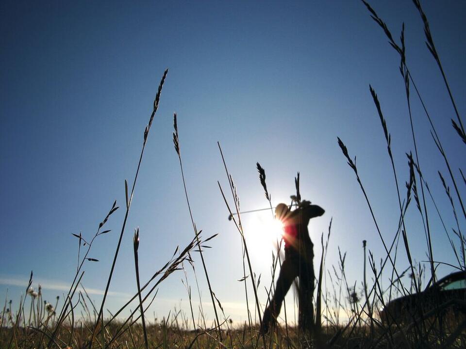 Silhouette of man playing golf against backdrop of sunshine and blue sky