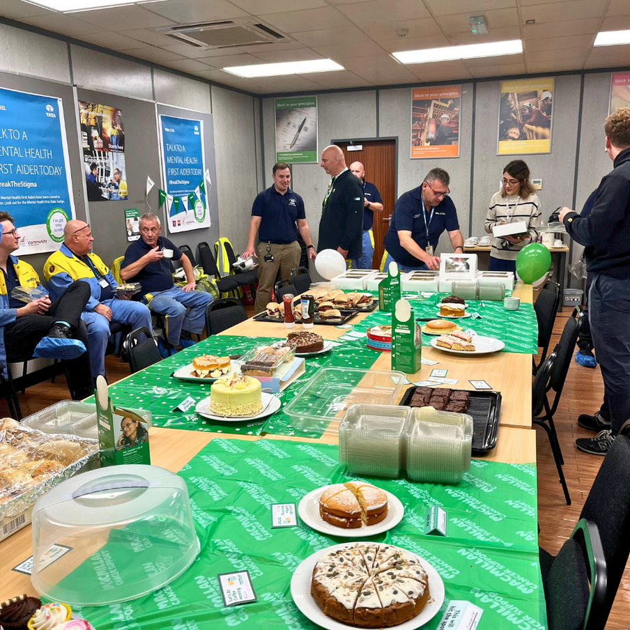 Table of cakes with steelworkers crowded around eating bakes